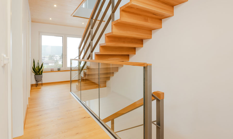 freitragende Faltwerktreppe aus Massivholz, Brüstungsgeländer aus Stahl und Glas, Handlauf in Massivholz